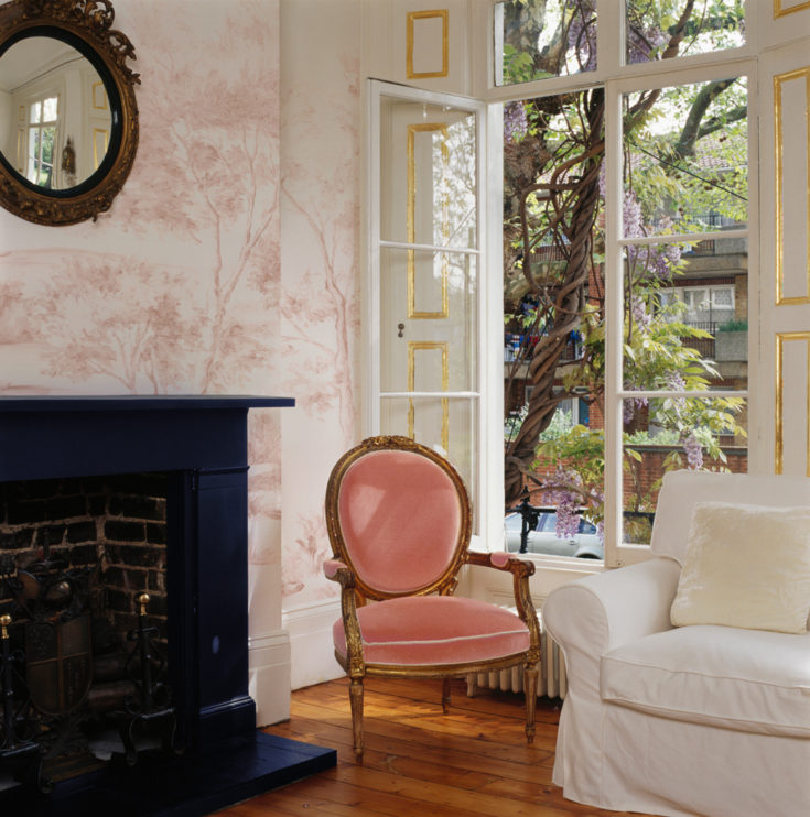 Delft Blush painted mural wallpaper in traditional french decor with a coral chair at a tall window.