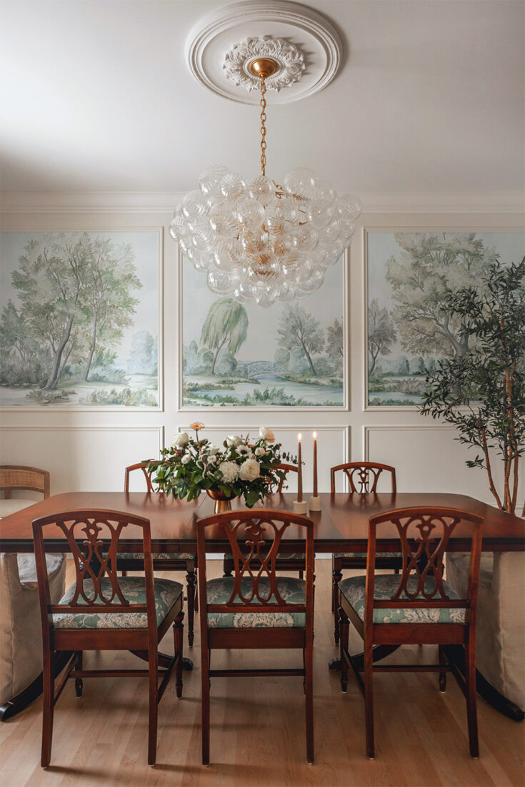 Blue colored landscape scenic mural wallpaper in panels framed my mouldings in an elegant dining room